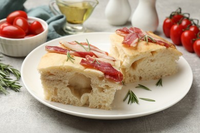 Photo of Pieces of delicious focaccia bread with bacon served on grey table, closeup