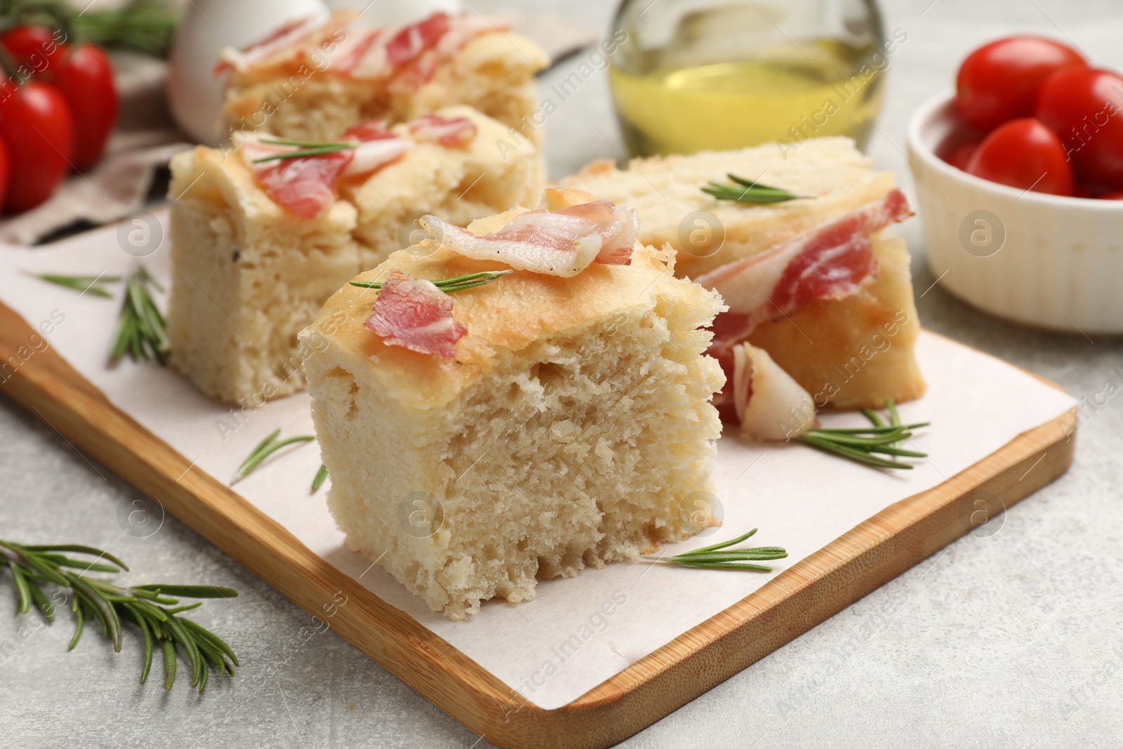 Photo of Pieces of delicious focaccia bread with bacon served on grey table, closeup