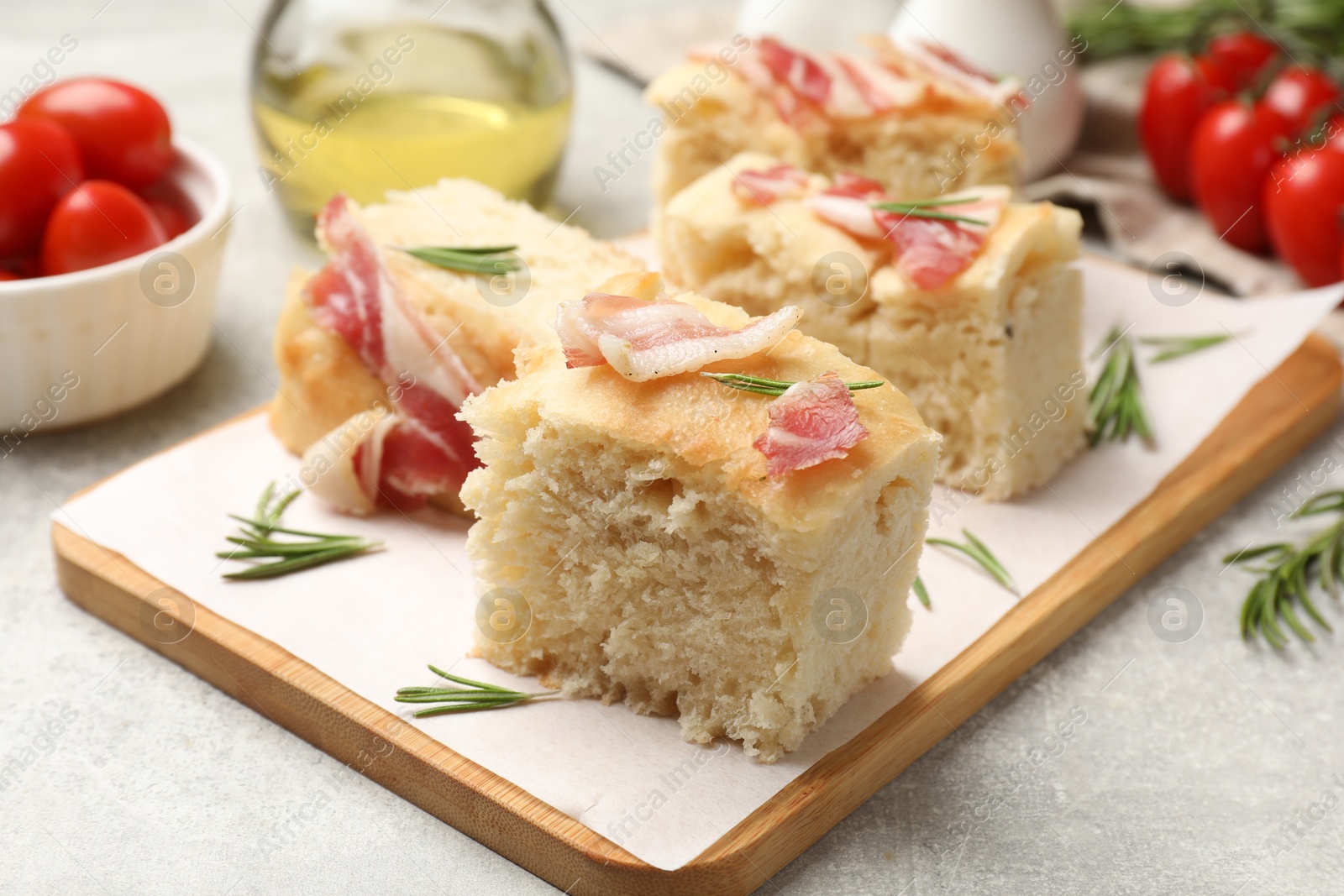 Photo of Pieces of delicious focaccia bread with bacon served on grey table, closeup