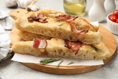 Photo of Pieces of delicious focaccia bread with bacon served on grey table, closeup