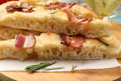 Photo of Pieces of delicious focaccia bread with bacon and rosemary on wooden board, closeup