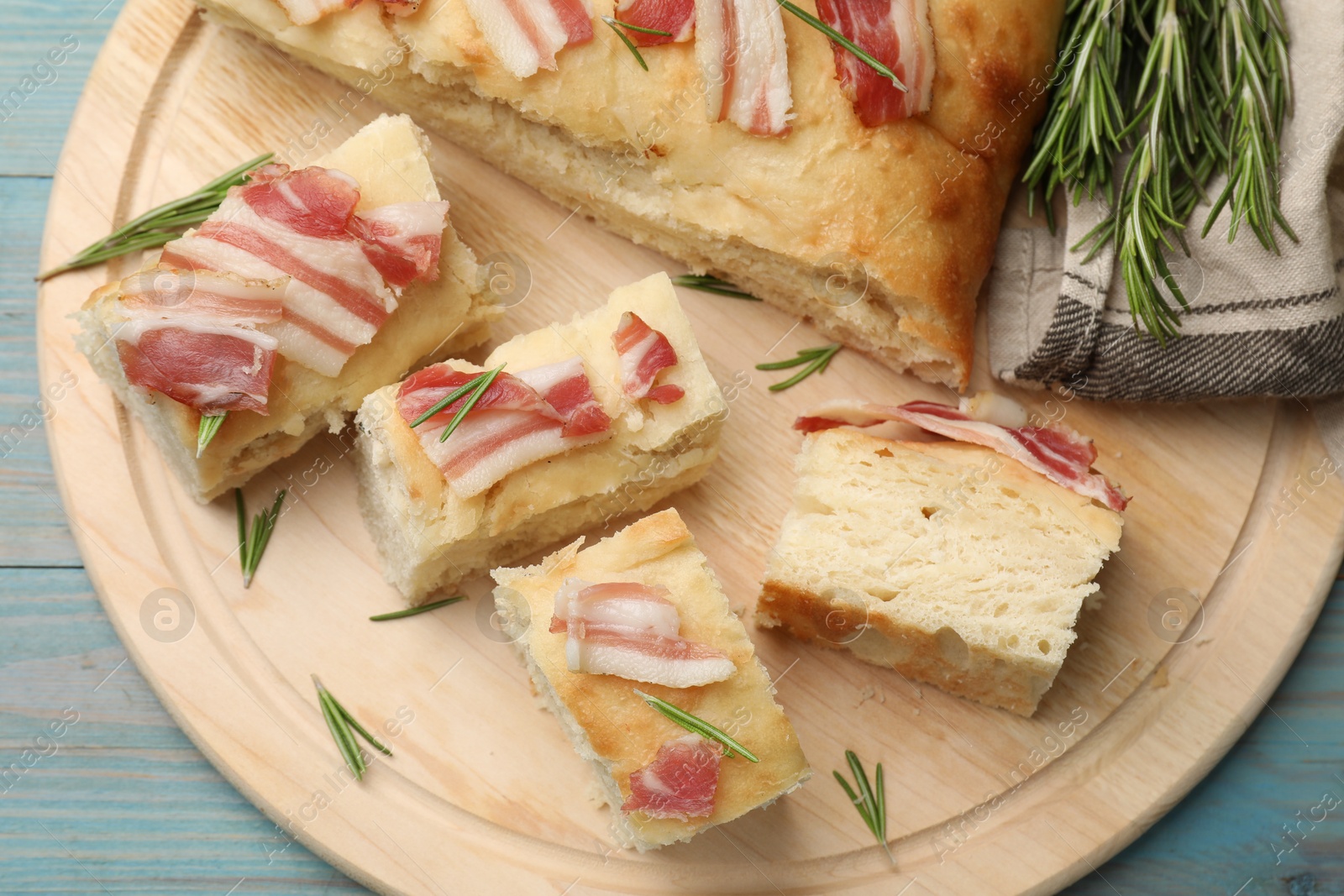 Photo of Pieces of delicious focaccia bread with bacon served on blue wooden table, top view