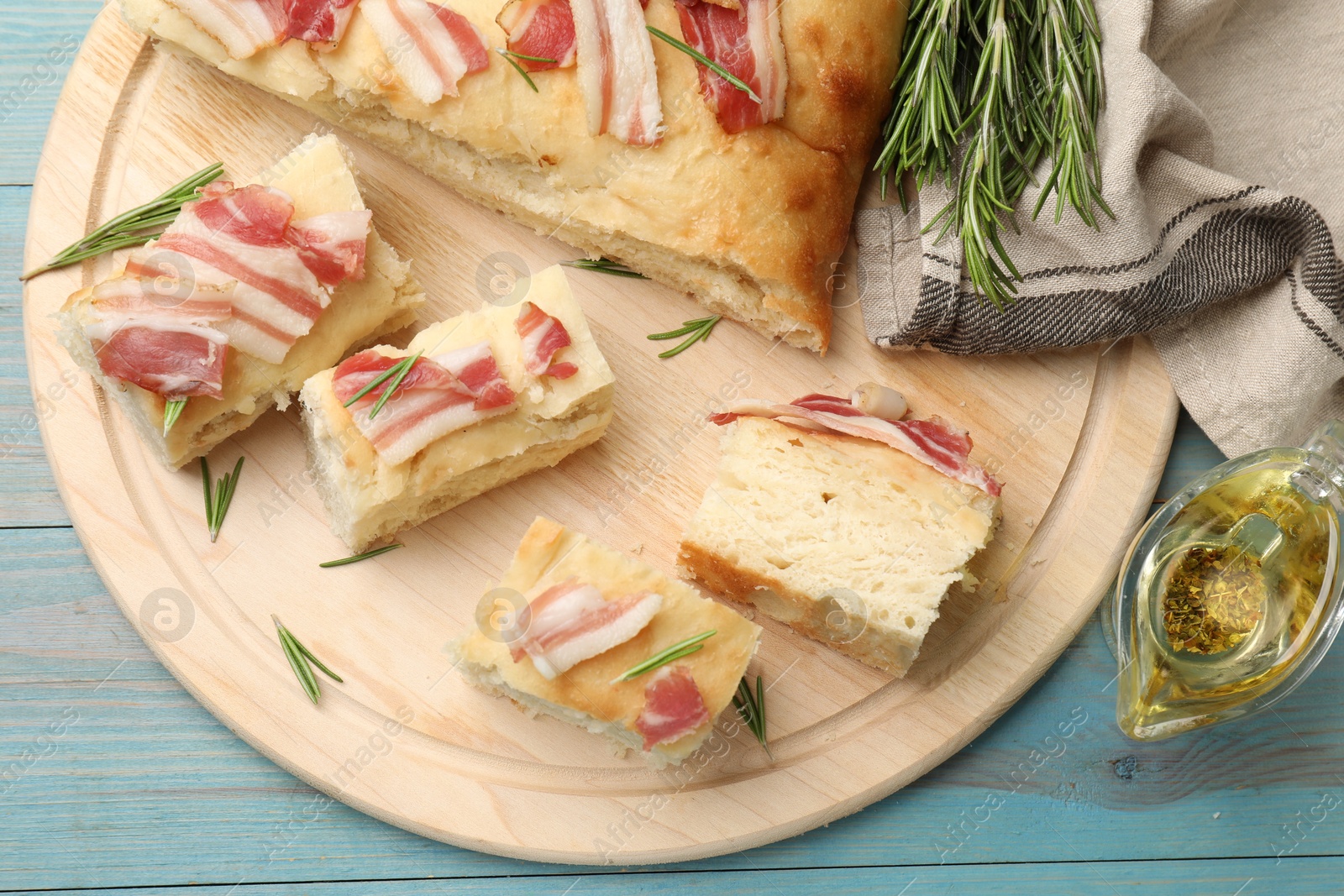 Photo of Pieces of delicious focaccia bread with bacon served on blue wooden table, flat lay