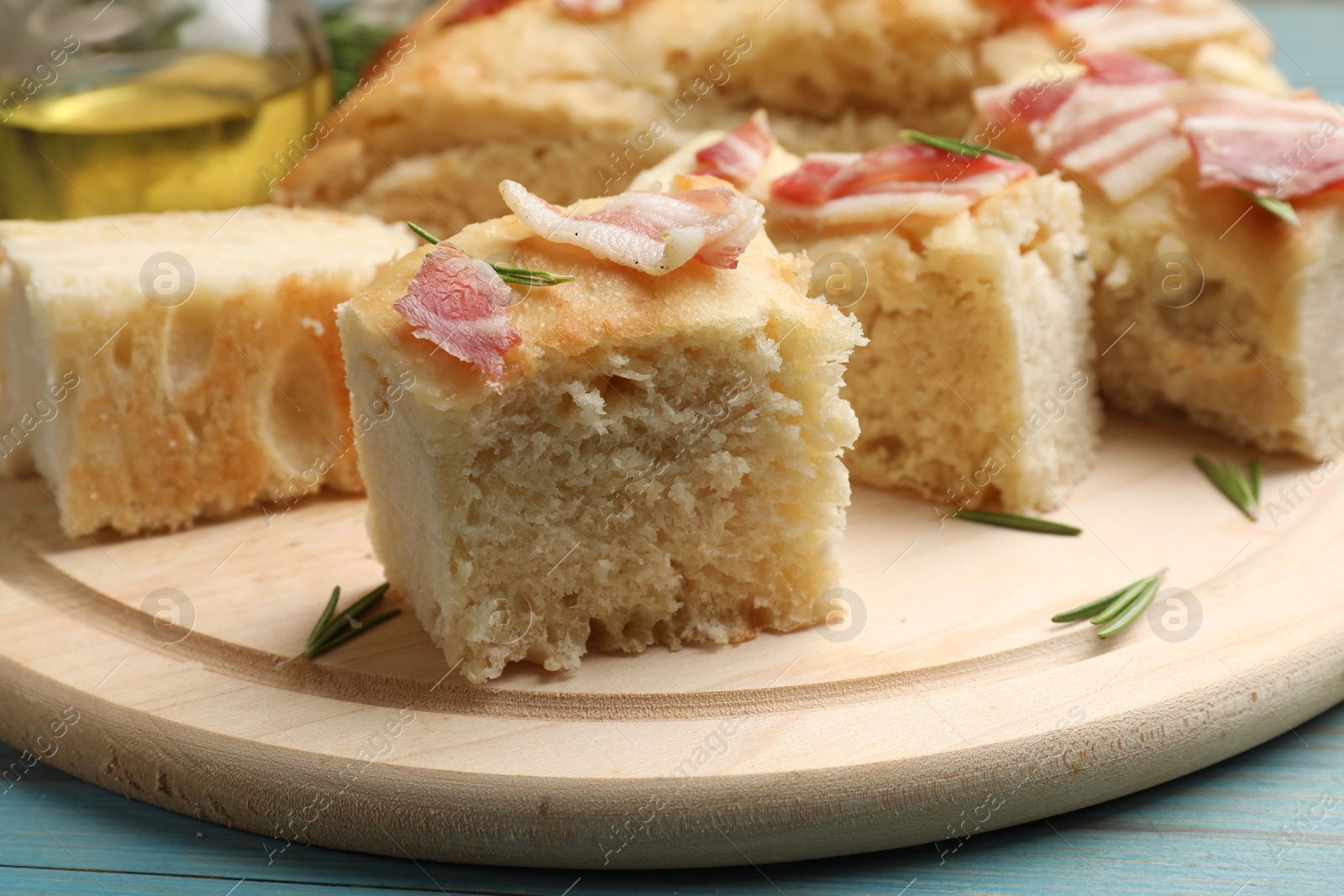 Photo of Pieces of delicious focaccia bread with bacon served on blue wooden table, closeup