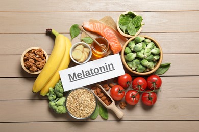 Photo of Word Melatonin and different products on wooden table, flat lay