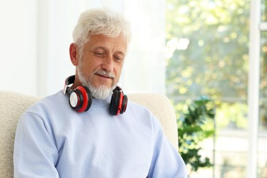 Photo of Senior man with headphones at home, space for text