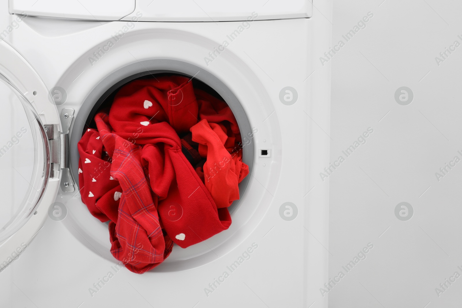 Photo of Washing machine with laundry near light wall, closeup