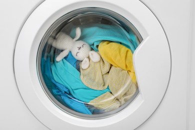 Photo of Washing machine with clothes and toy bunny as background, closeup