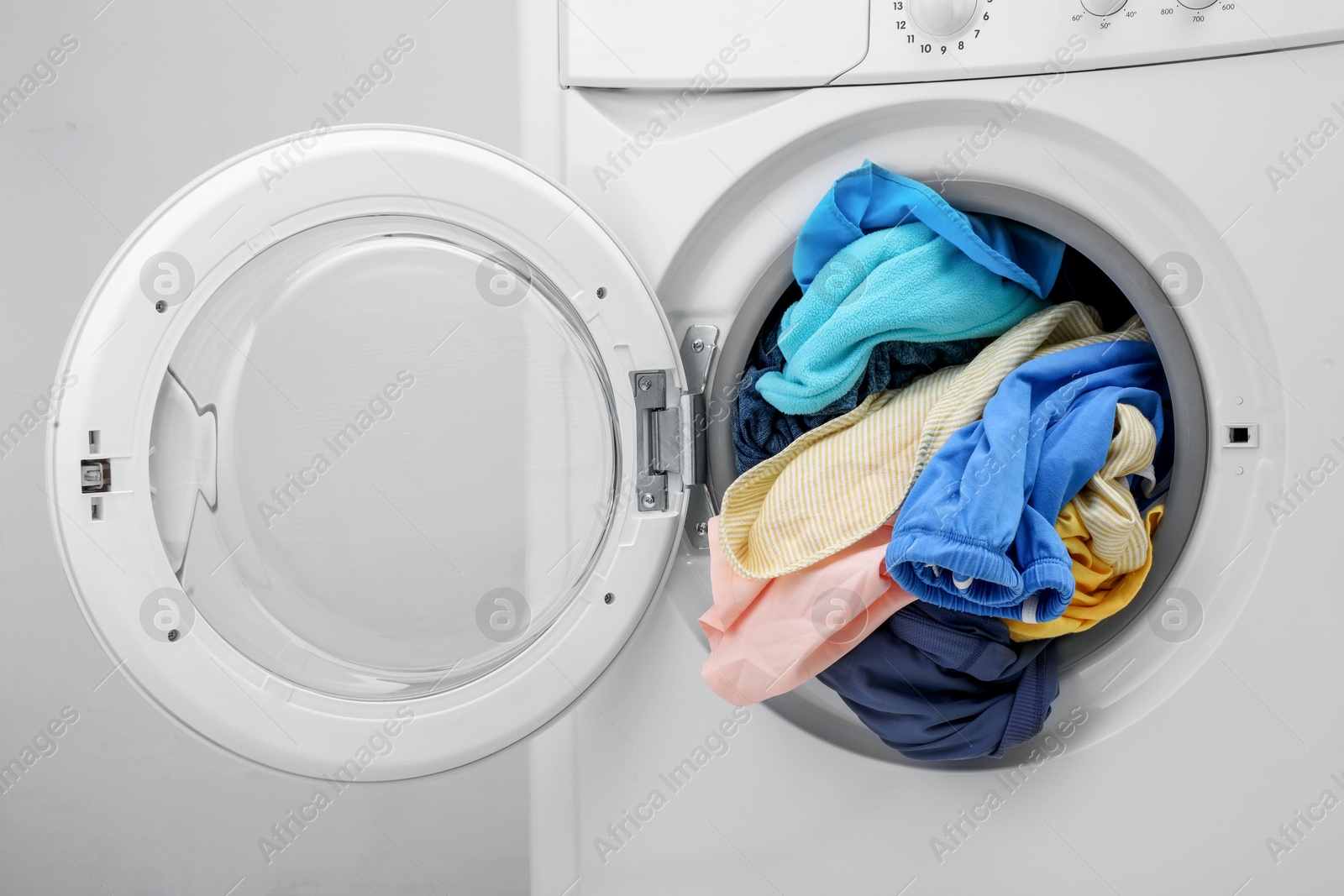 Photo of Washing machine with laundry near light wall, closeup