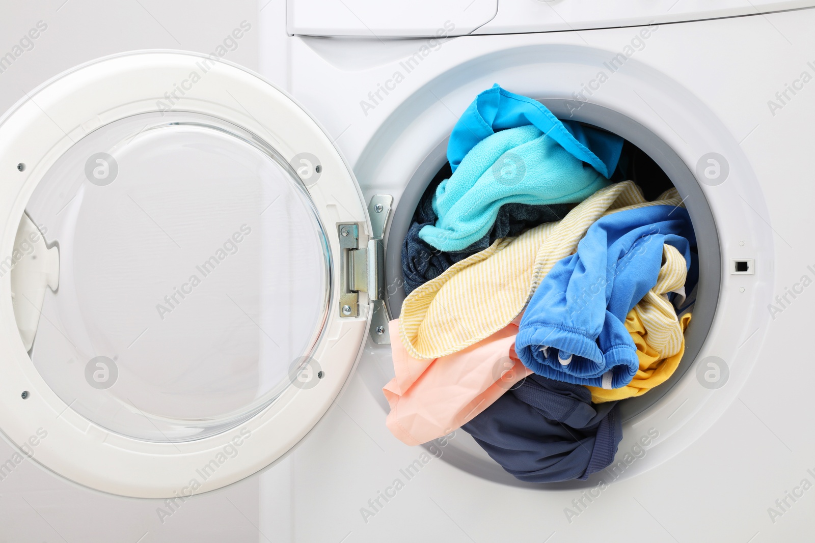 Photo of Washing machine with laundry near light wall, closeup