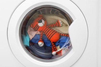 Photo of Washing machine with clothes and toy tiger as background, closeup