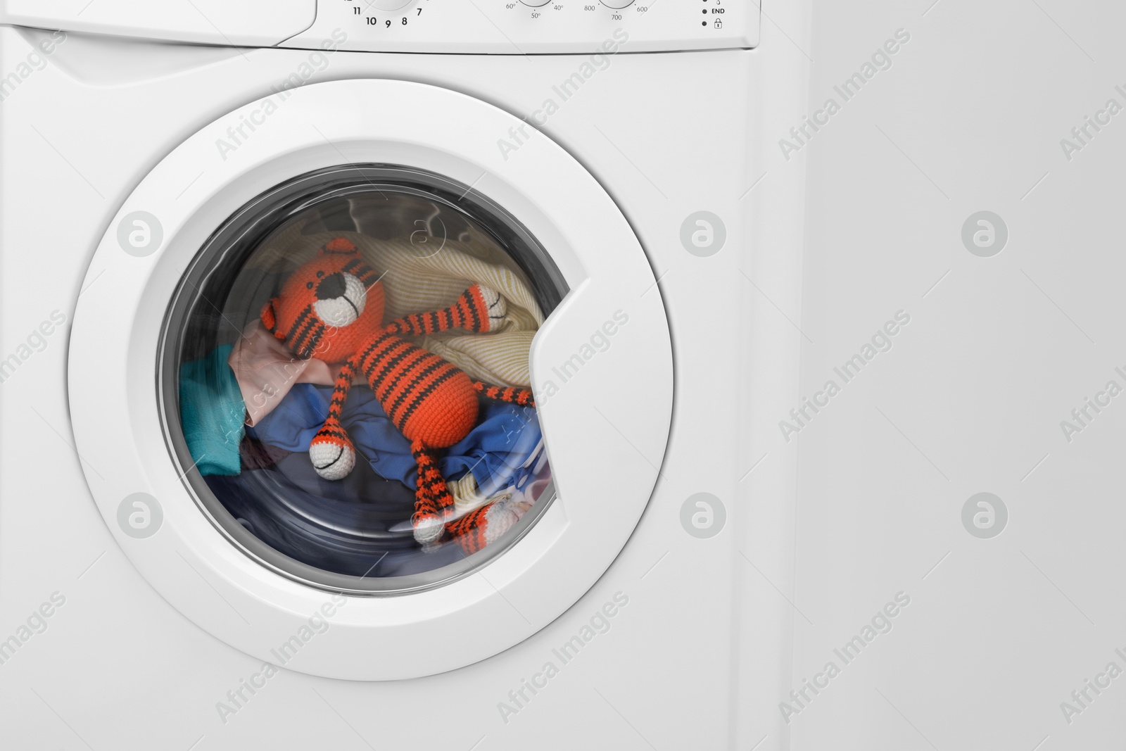 Photo of Washing machine with clothes and toy tiger near light wall, closeup