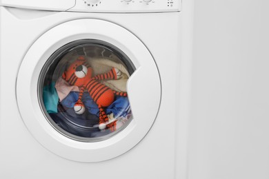 Photo of Washing machine with clothes and toy tiger near light wall, closeup