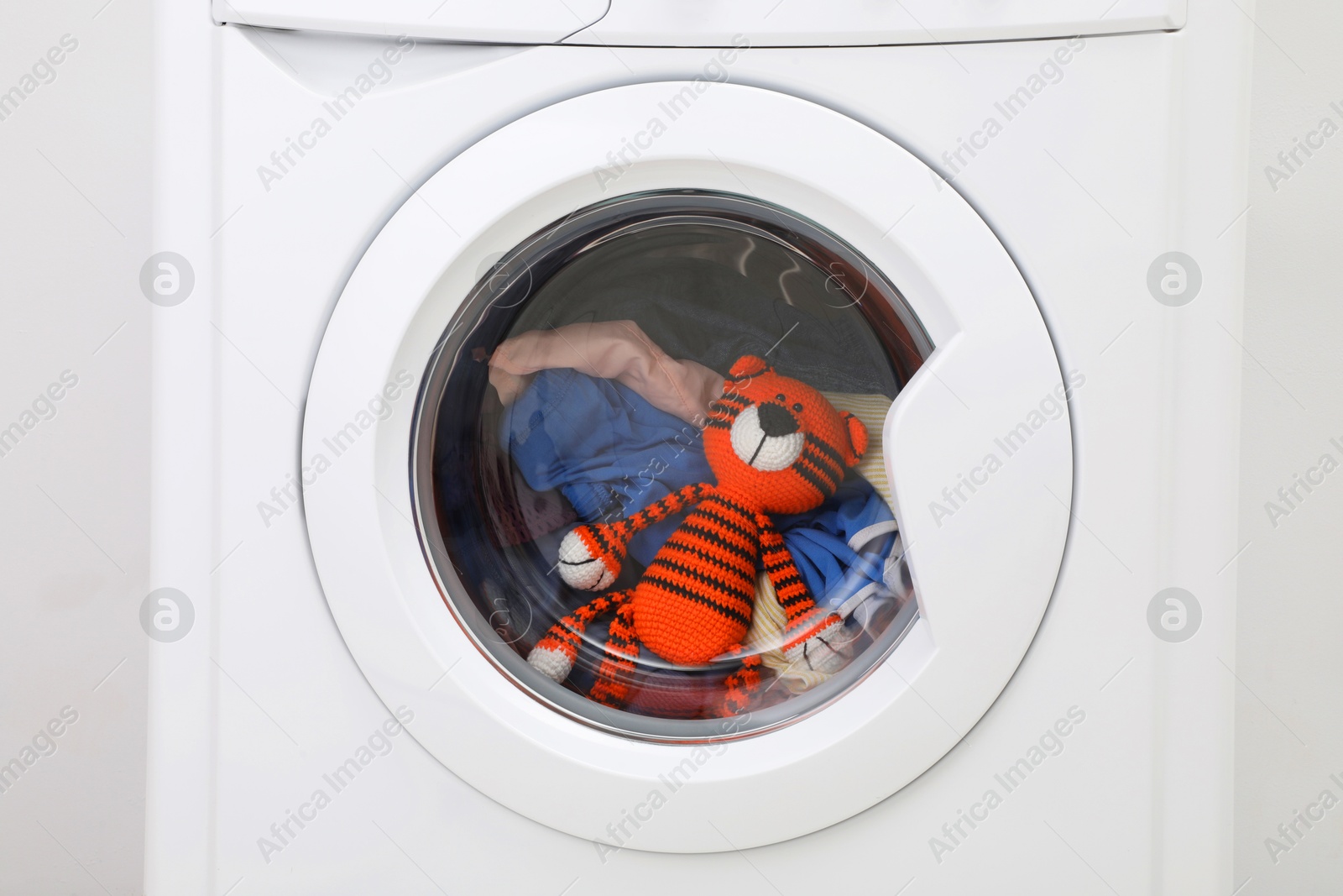 Photo of Washing machine with clothes and toy tiger as background, closeup