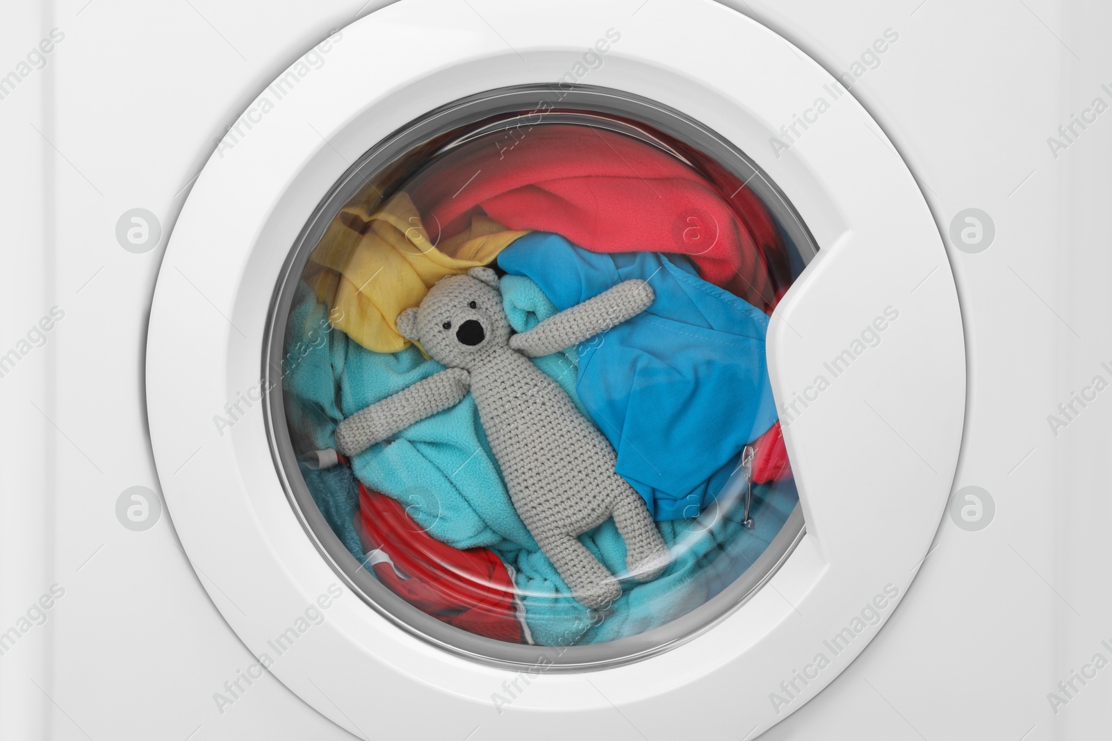 Photo of Washing machine with clothes and toy bear as background, closeup