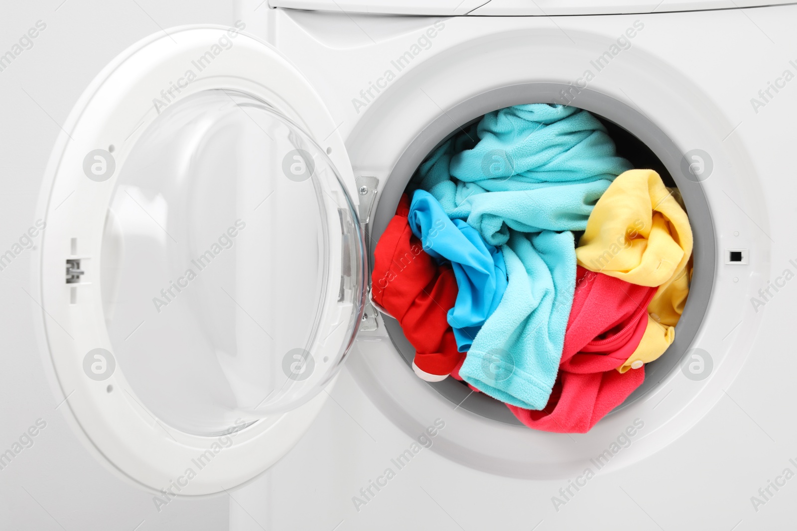 Photo of Washing machine with laundry near light wall, closeup