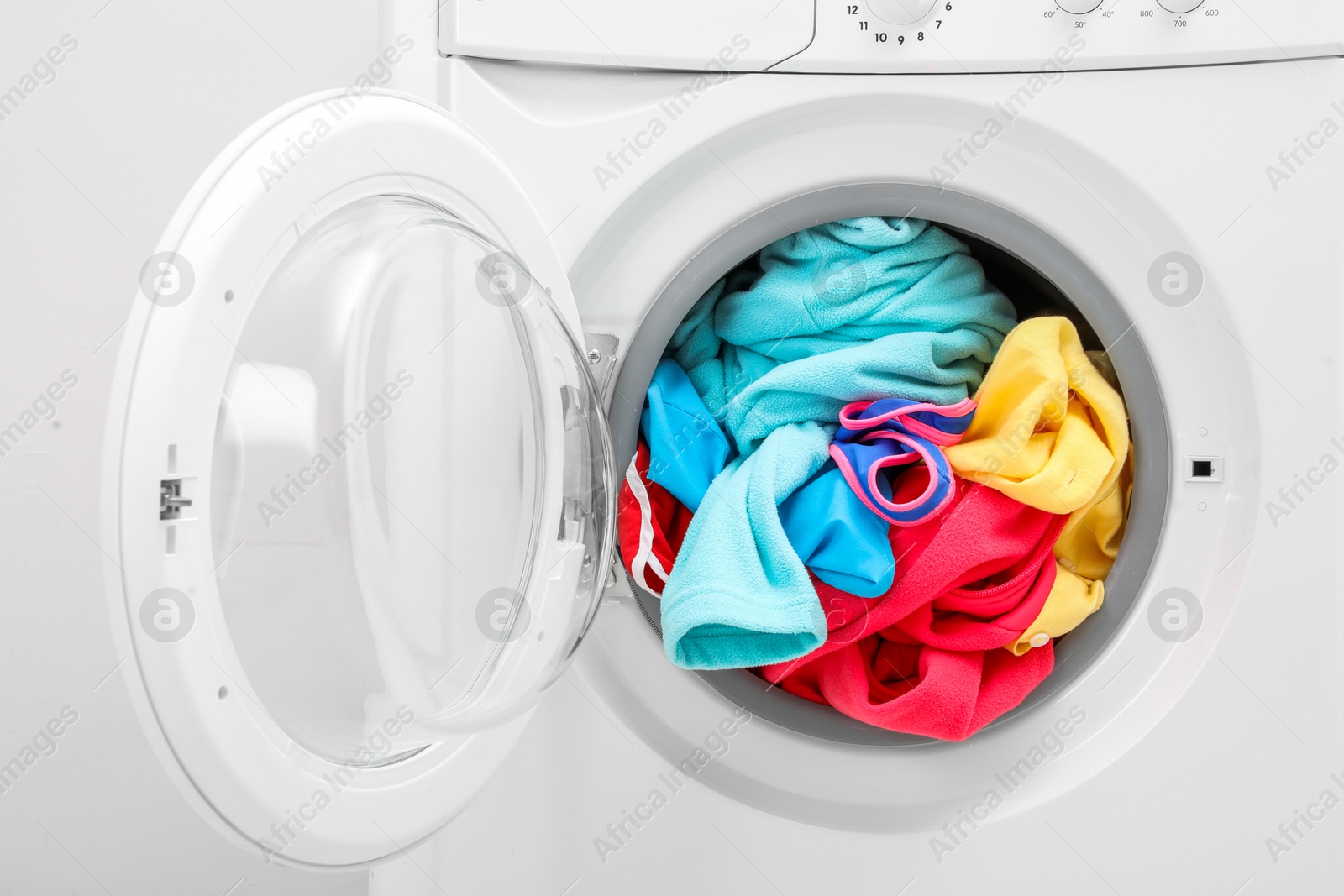 Photo of Washing machine with laundry near light wall, closeup