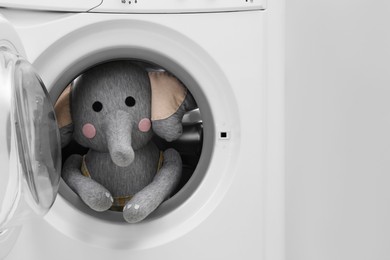 Photo of Washing machine with toy elephant near light wall, closeup