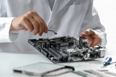 Photo of Man installing computer chip onto motherboard at white table, closeup