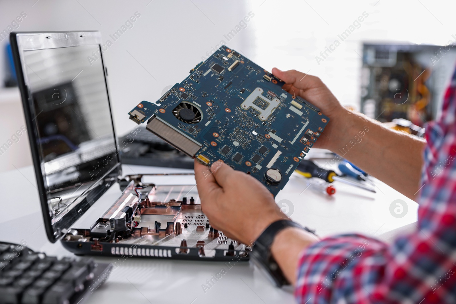 Photo of Man installing motherboard into laptop at white table, closeup