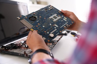 Photo of Man installing motherboard into laptop at white table, closeup