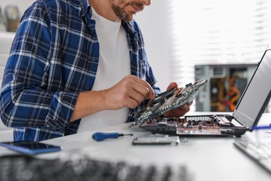 Photo of Man installing motherboard into laptop at white table, closeup