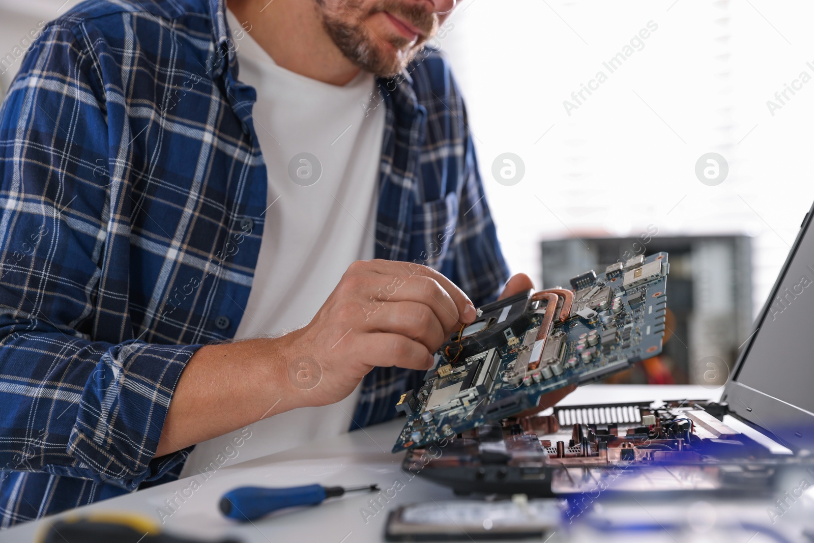 Photo of Man installing motherboard into laptop at white table, closeup