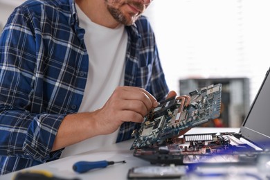 Photo of Man installing motherboard into laptop at white table, closeup