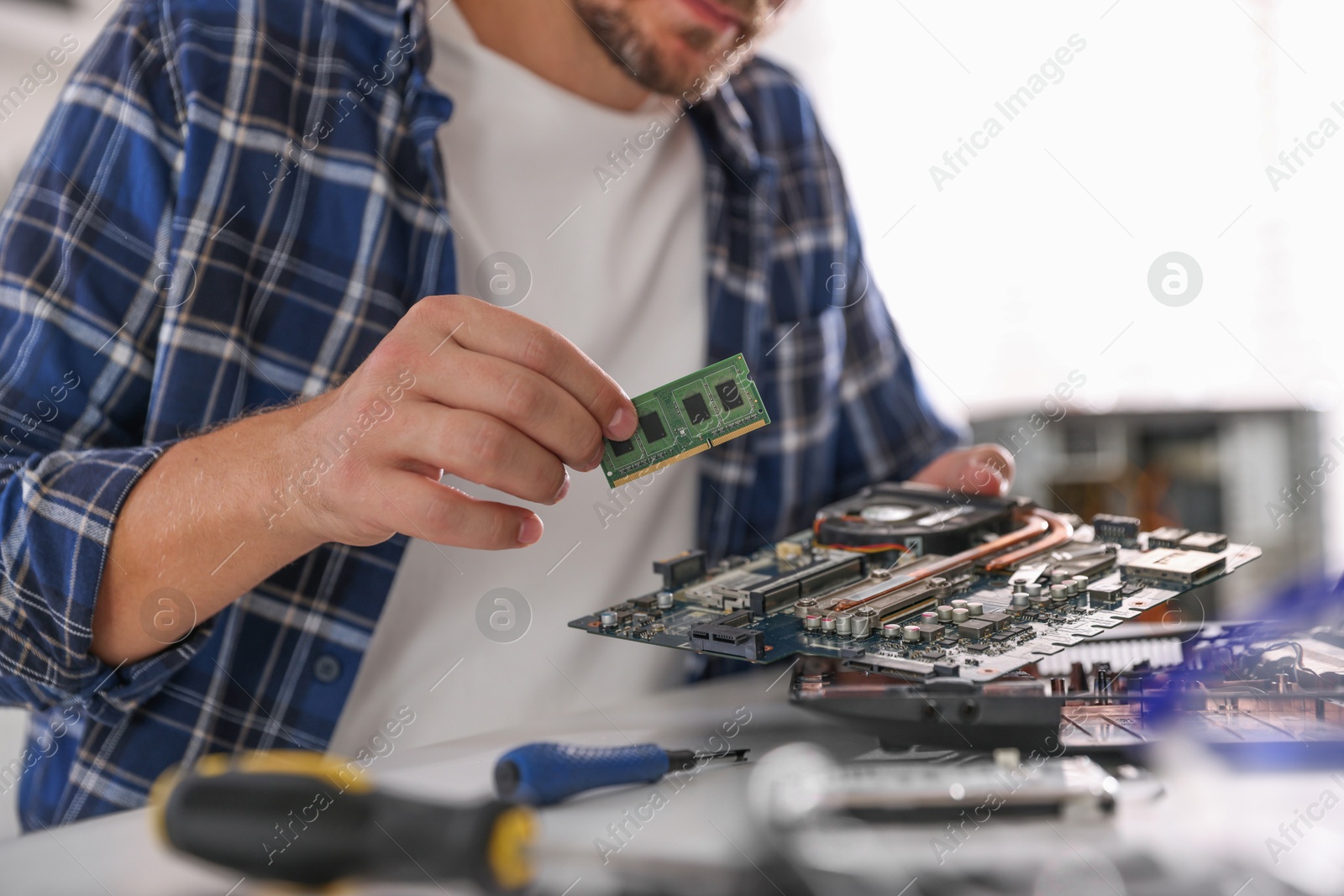 Photo of Man installing motherboard into laptop at white table, closeup