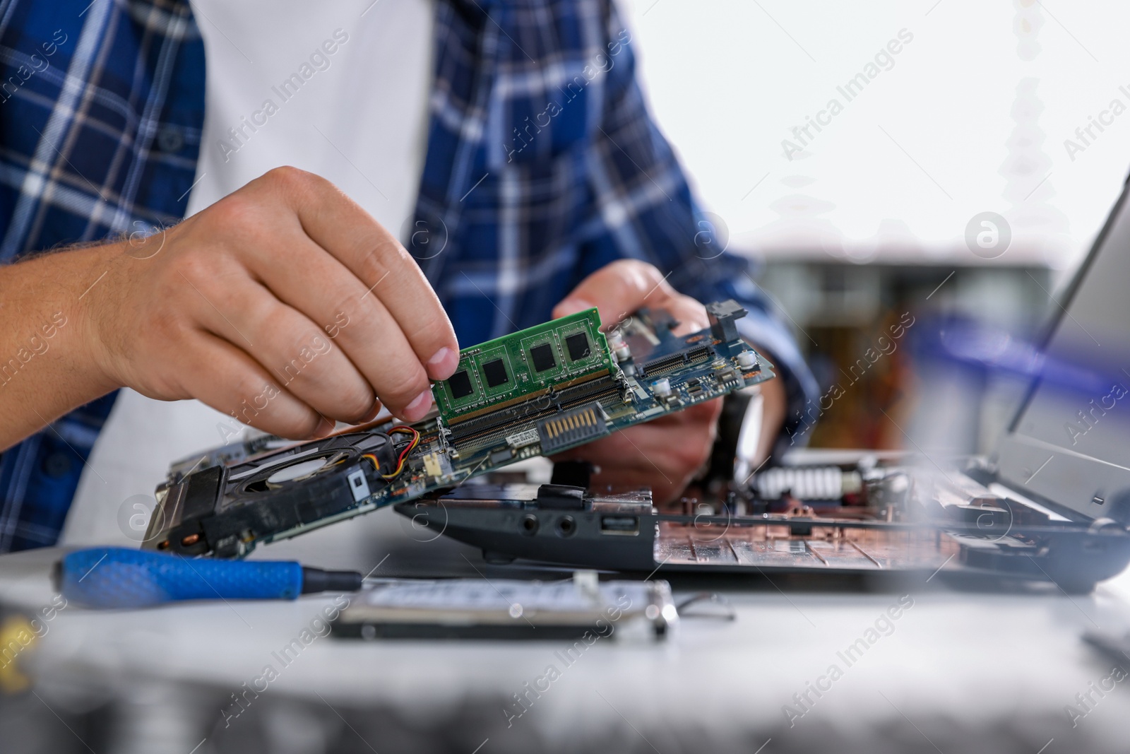 Photo of Man installing motherboard into laptop at white table, closeup