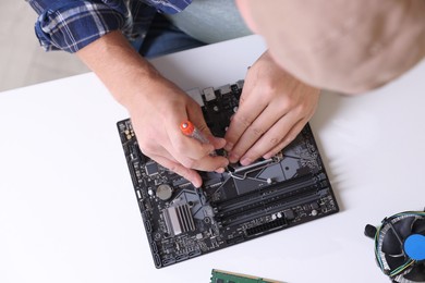 Photo of Man installing computer chip onto motherboard at white table, top view