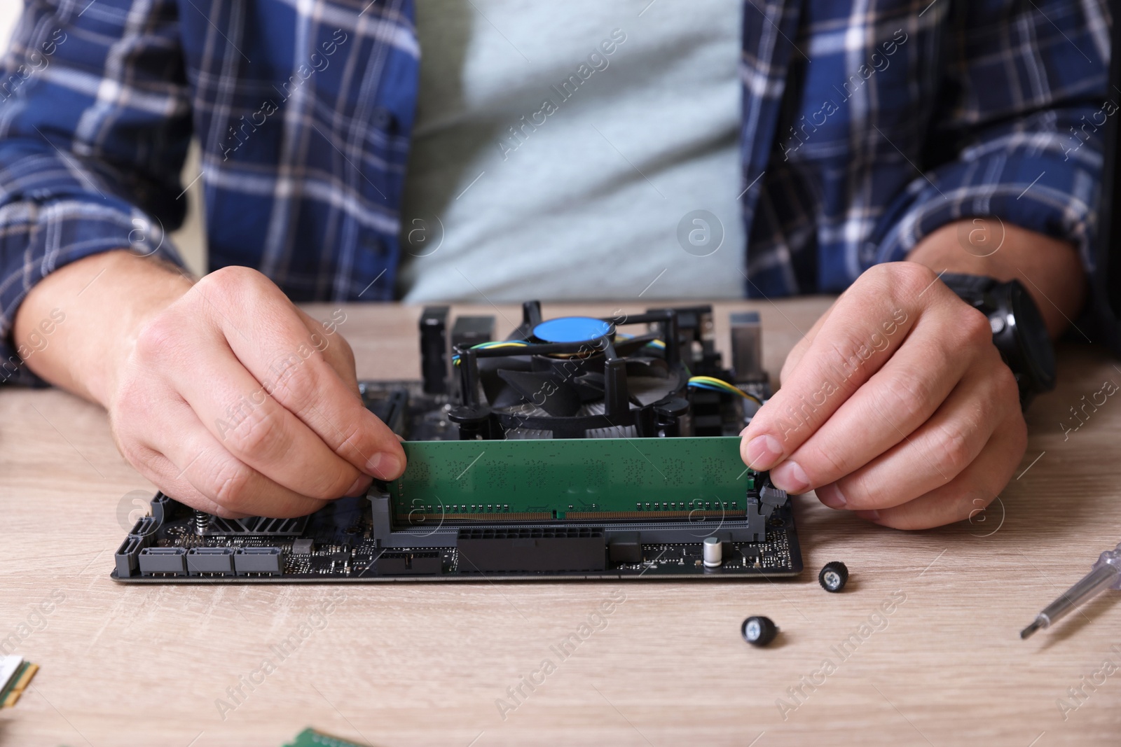 Photo of Man installing computer chip onto motherboard at wooden table, closeup