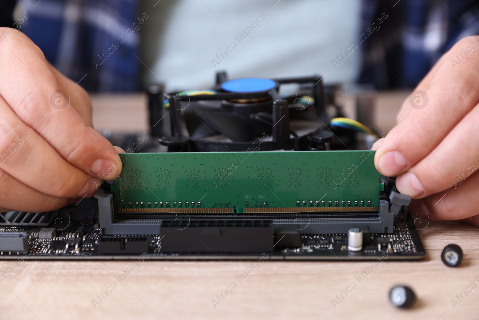 Photo of Man installing computer chip onto motherboard at wooden table, closeup