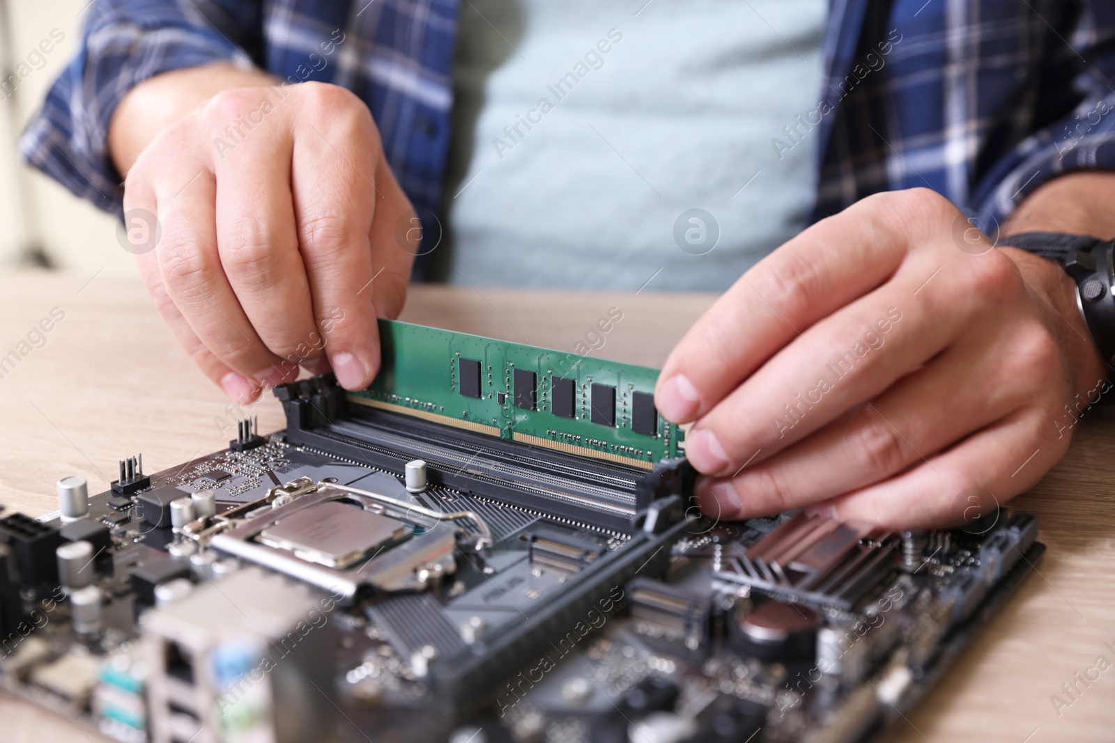 Photo of Man installing computer chip onto motherboard at wooden table, closeup