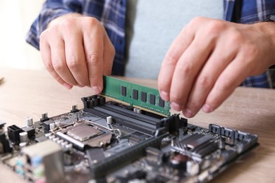 Photo of Man installing computer chip onto motherboard at wooden table, closeup