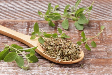 Dried oregano in spoon and green leaves on wooden table, closeup