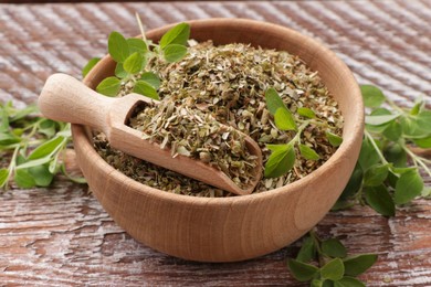 Photo of Dried oregano in bowl, scoop and green leaves on wooden table, closeup