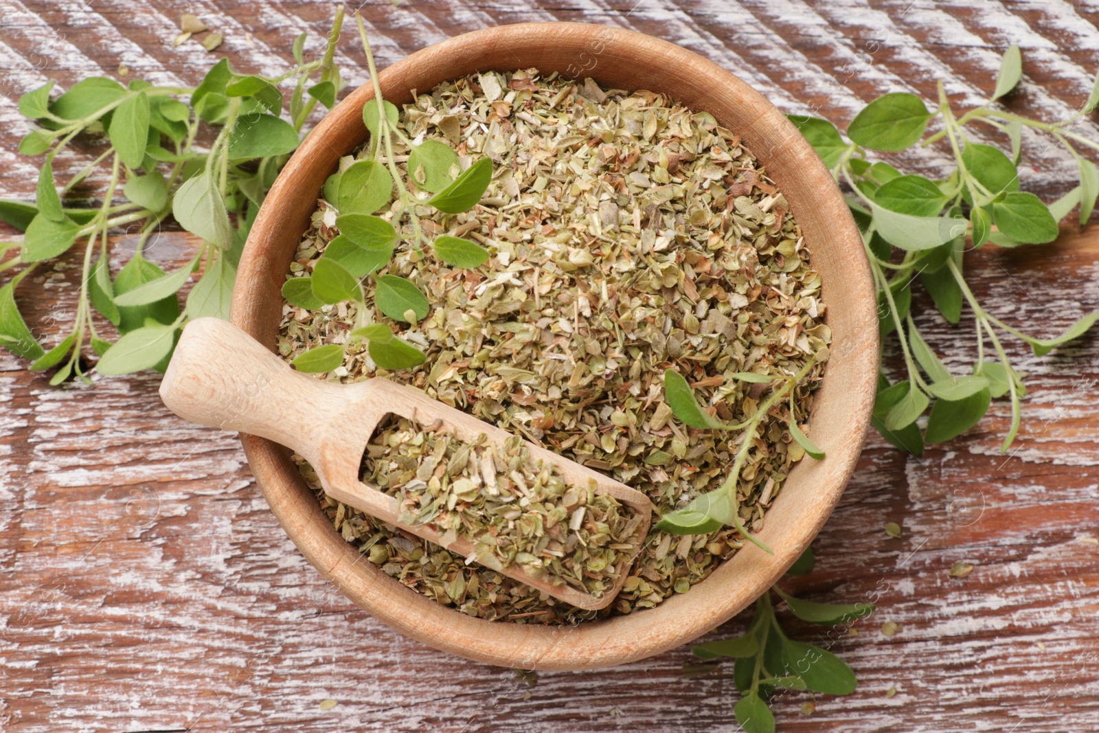 Photo of Dried oregano in bowl, scoop and green leaves on wooden table, top view