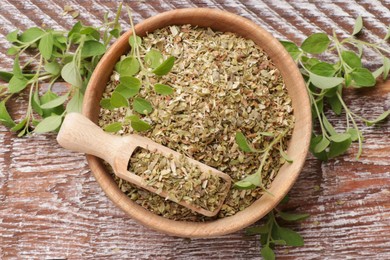 Photo of Dried oregano in bowl, scoop and green leaves on wooden table, top view