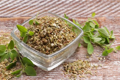 Photo of Dried oregano in glass jar and green leaves on wooden table, closeup