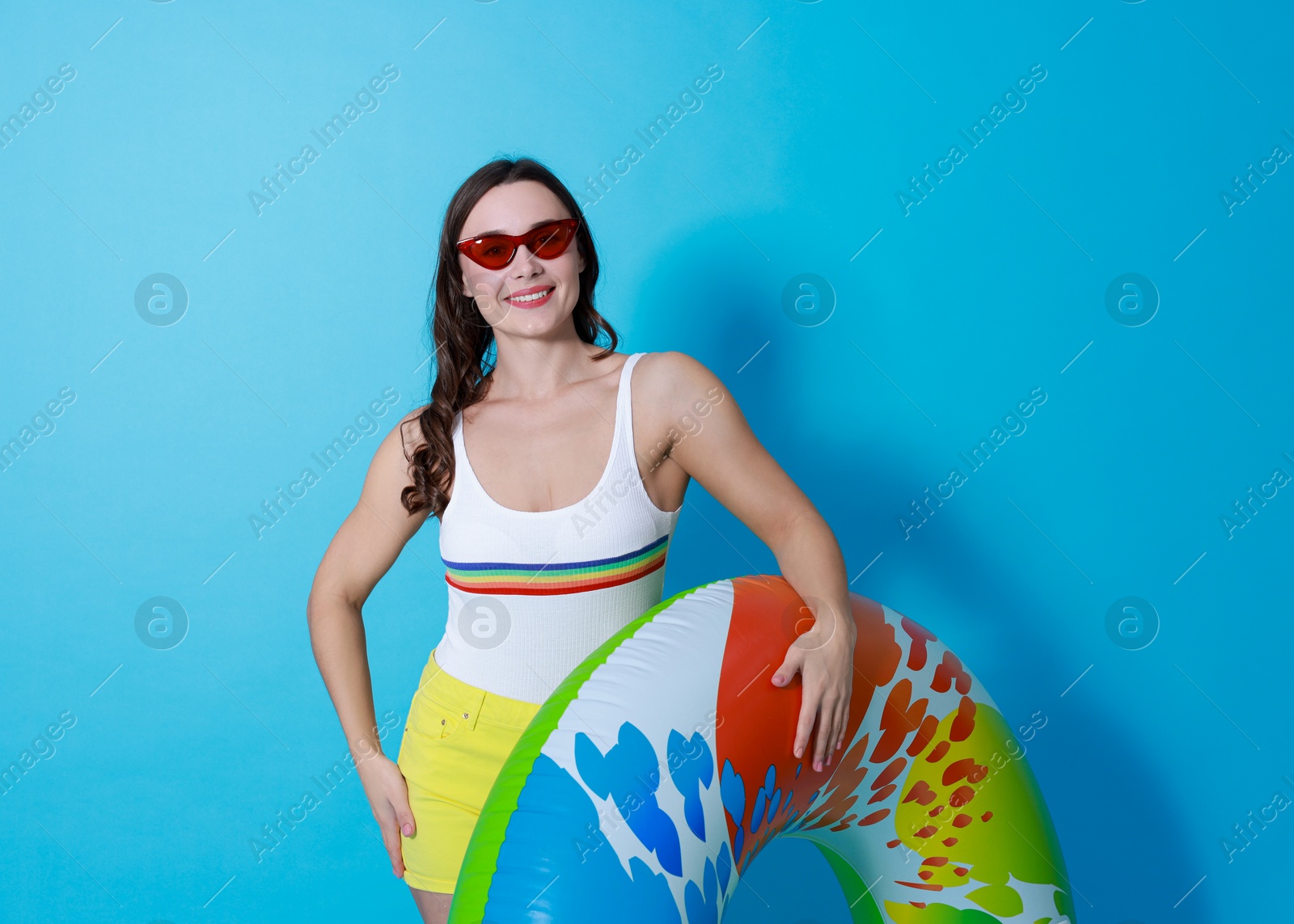 Photo of Beautiful woman in swimsuit with inflatable ring on light blue background