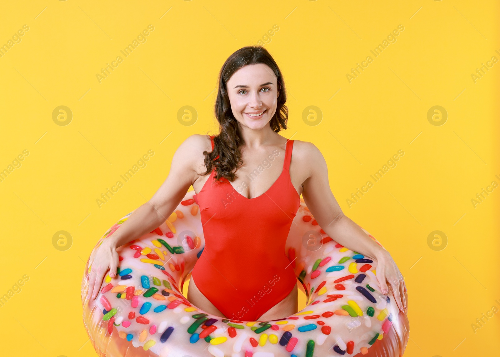 Photo of Beautiful woman in swimsuit with inflatable ring on yellow background