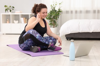 Photo of Plus size woman having fitness training with online coach via laptop at home