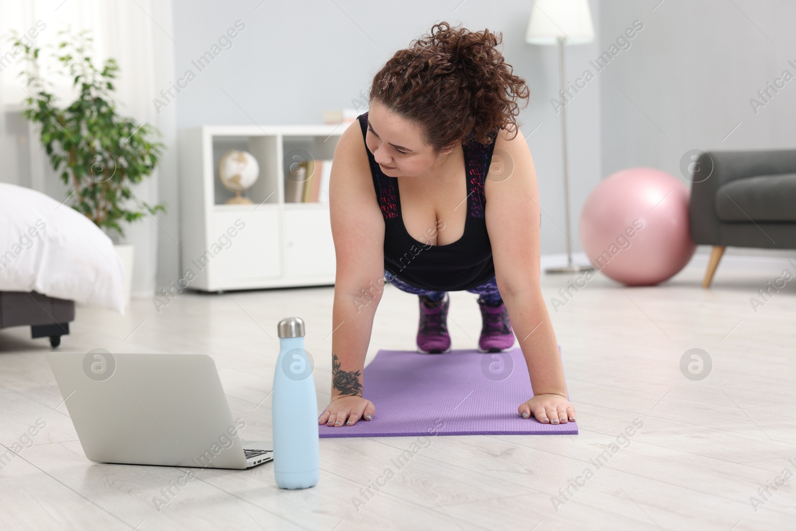 Photo of Plus size woman having fitness training with online coach via laptop at home