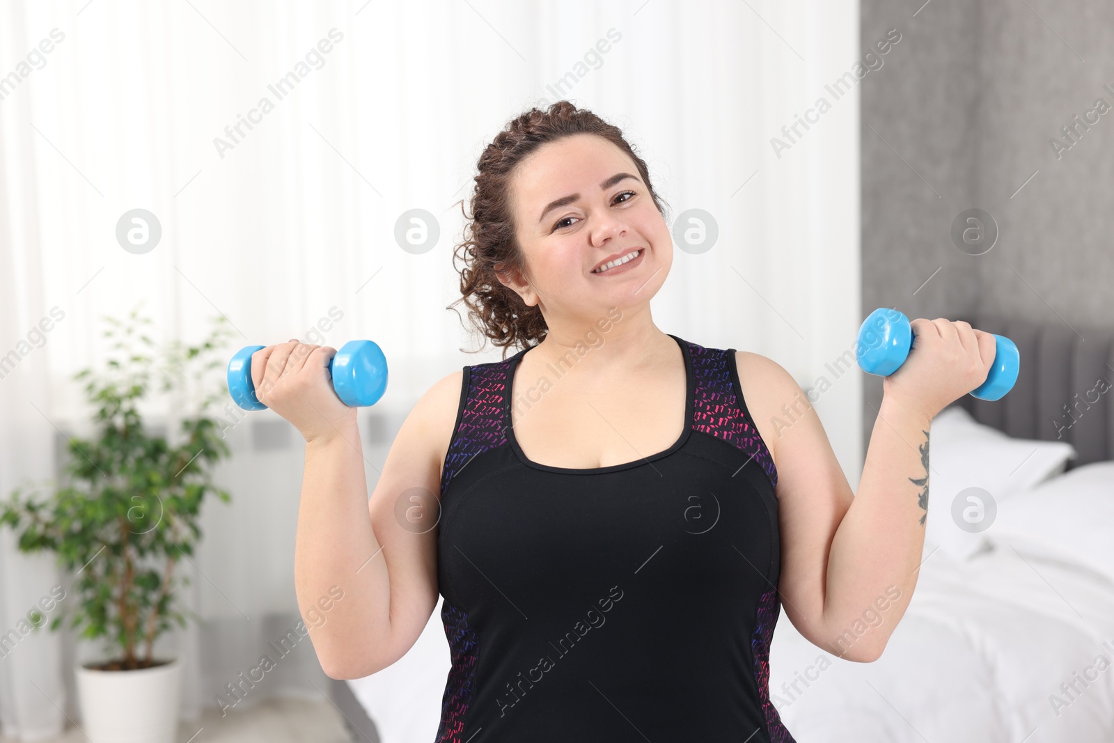 Photo of Plus size woman with dumbbells training at home