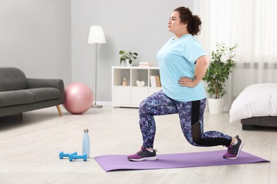 Photo of Plus size woman exercising on fitness mat at home