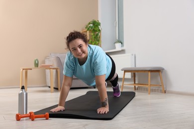 Photo of Woman doing plank exercise on fitness mat at home