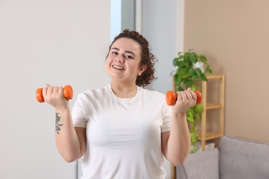 Photo of Plus size woman with dumbbells training at home