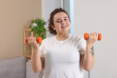 Photo of Plus size woman with dumbbells training at home