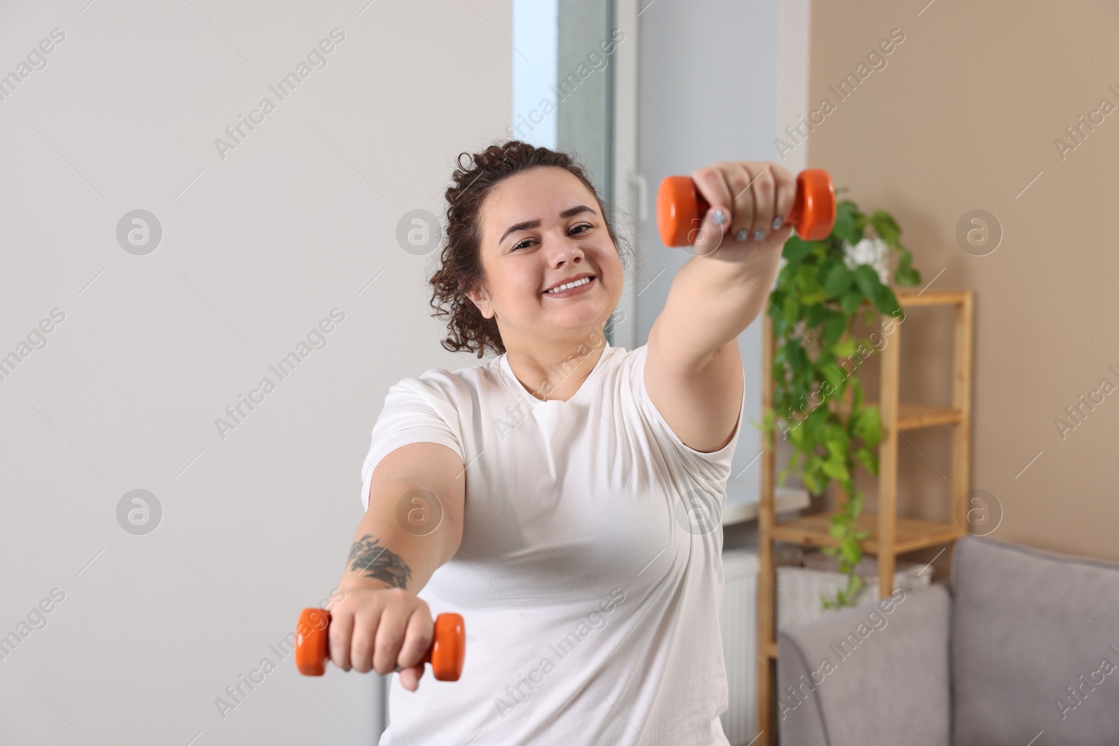 Photo of Plus size woman with dumbbells training at home